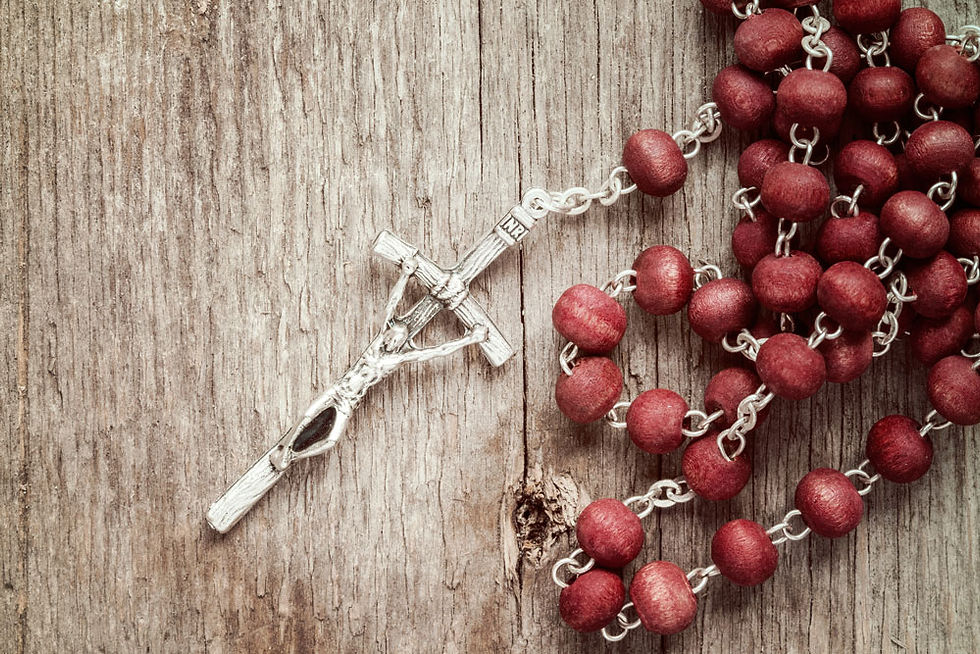A red wooden rosary with a silver crucifix sitting on a wooden table